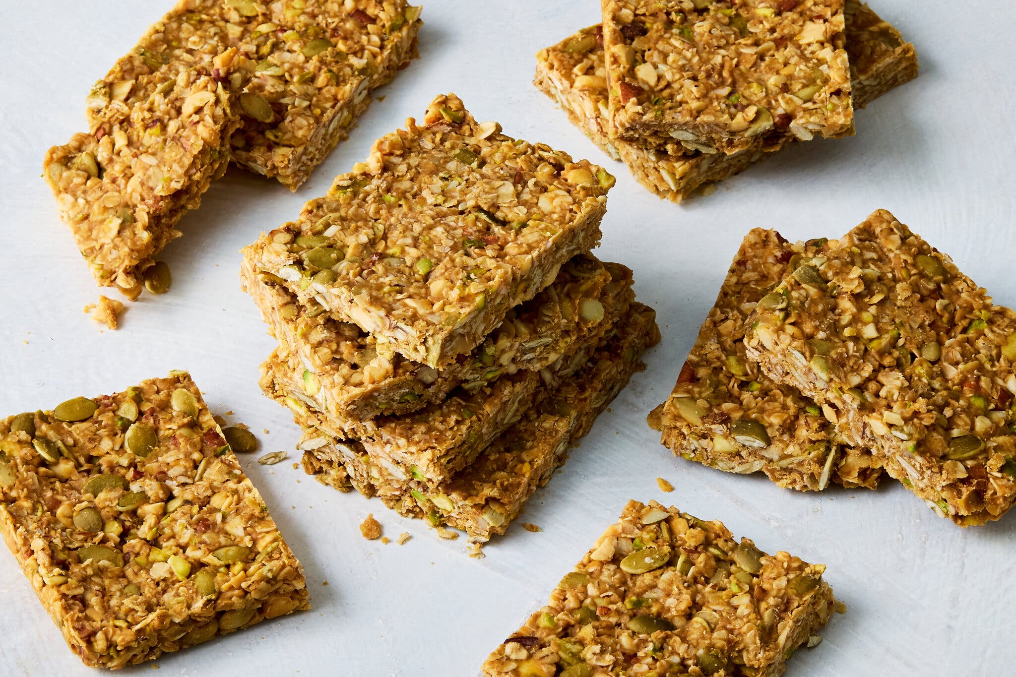 Several brown rectangles studded with oats and nuts are stacked and scattered around a white surface.