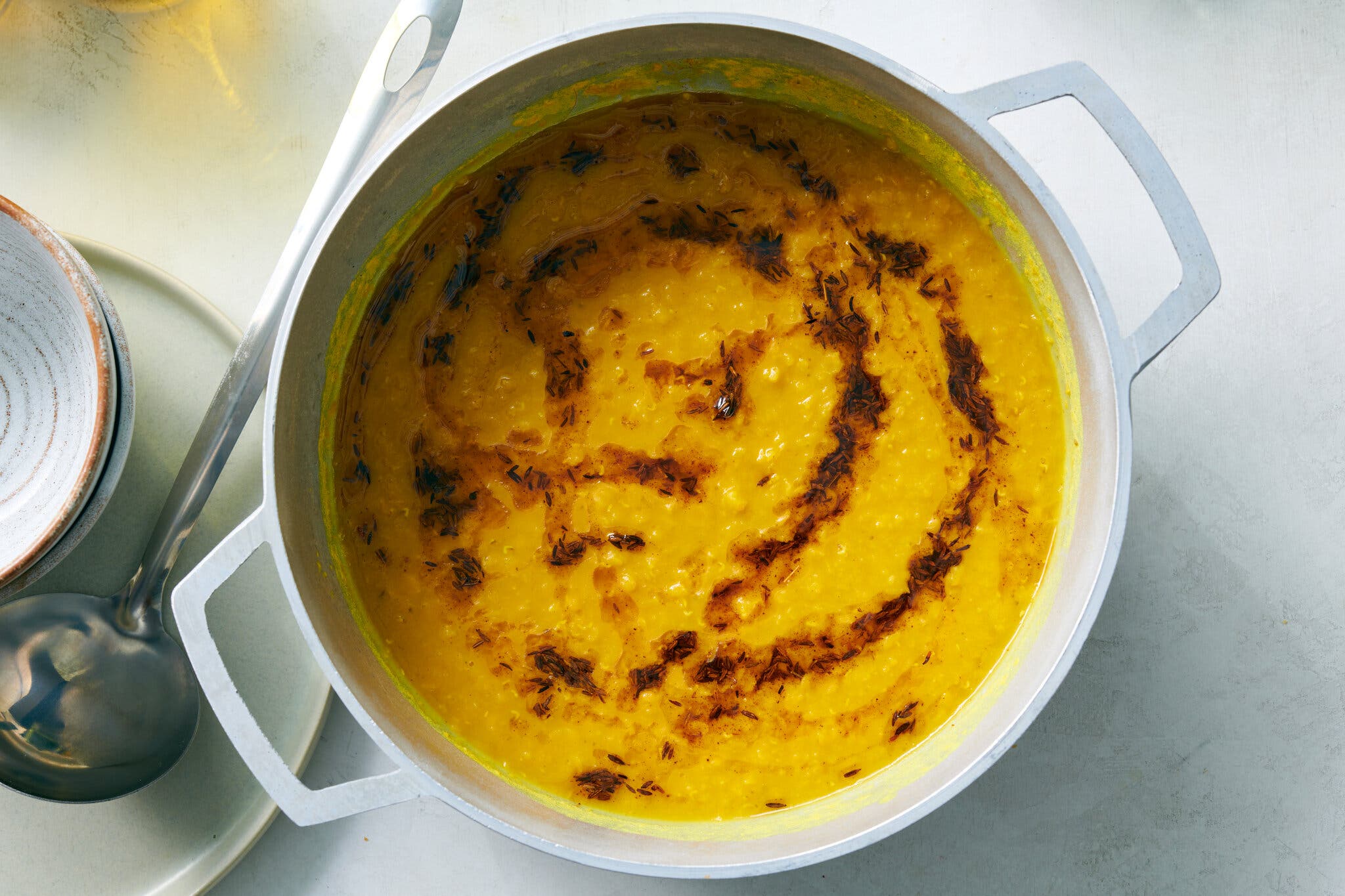 A large white handled pot with a deep golden soup inside drizzled with a brown spice mixture. 