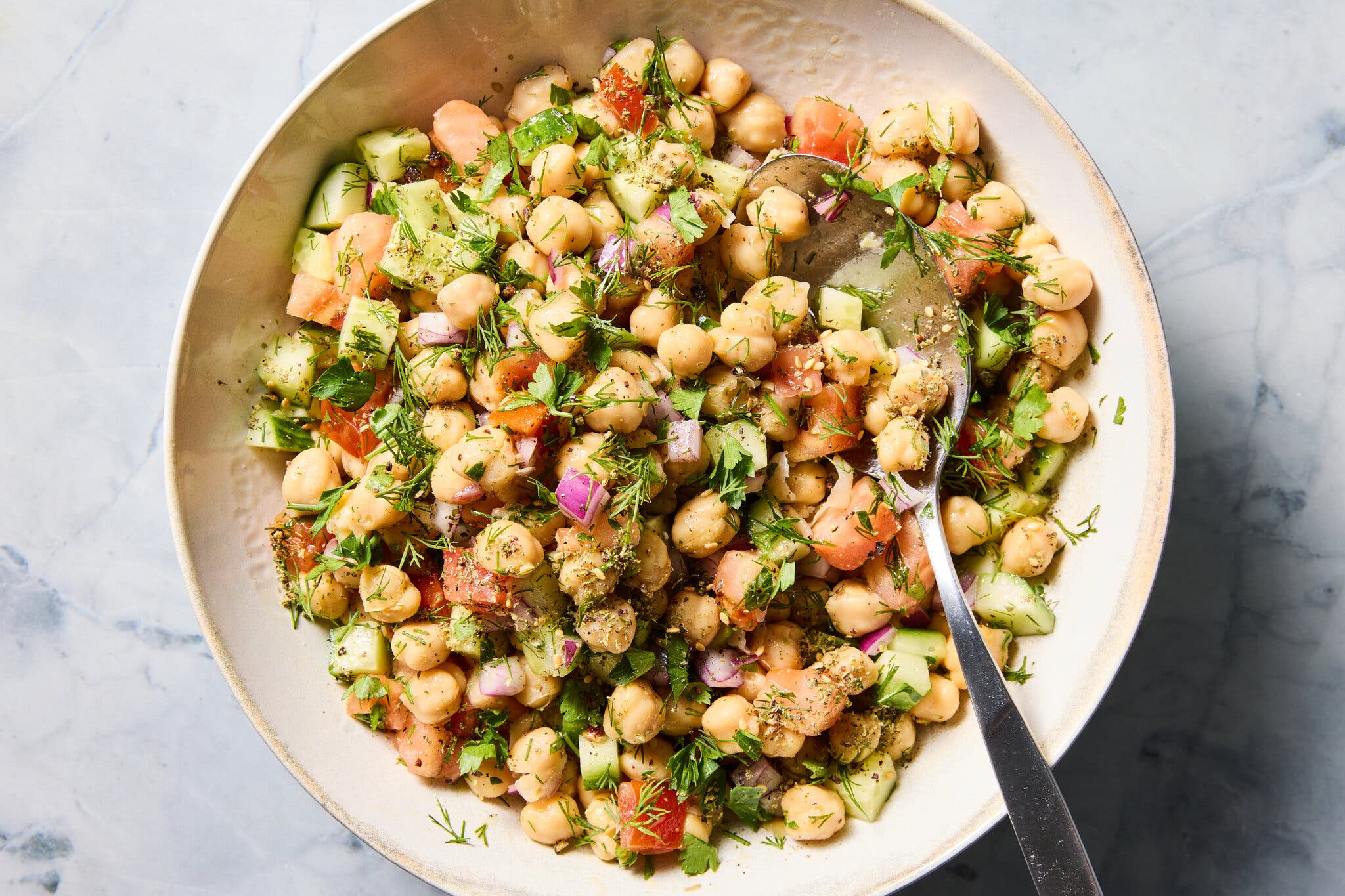 An overhead image of a beige bowl filled with chickpeas, tomatoes, red onion and herbs. 