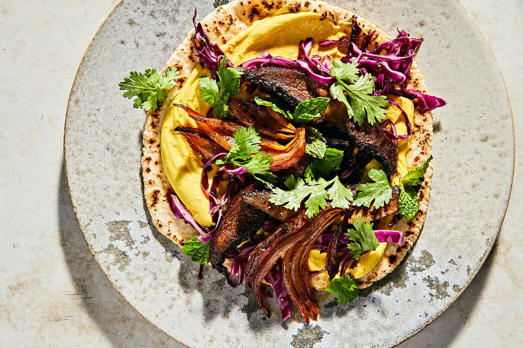 An overhead image of a pita topped with mushrooms, herbs and onions.