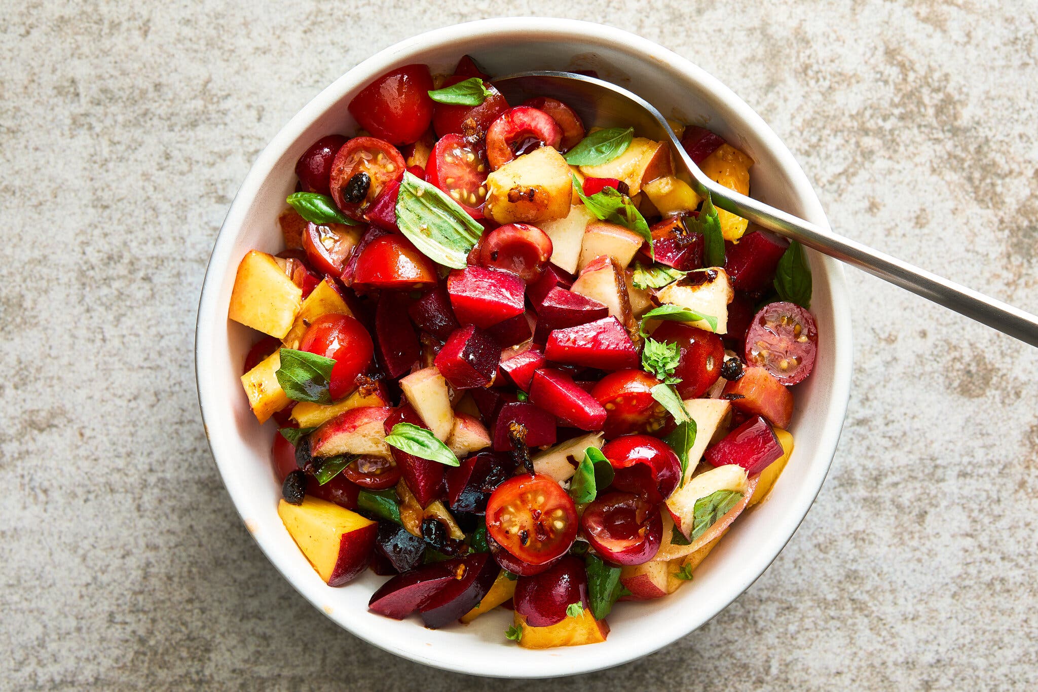 A serving bowl of summer fruit salad with tomatoes, basil and a spicy vinaigrette.