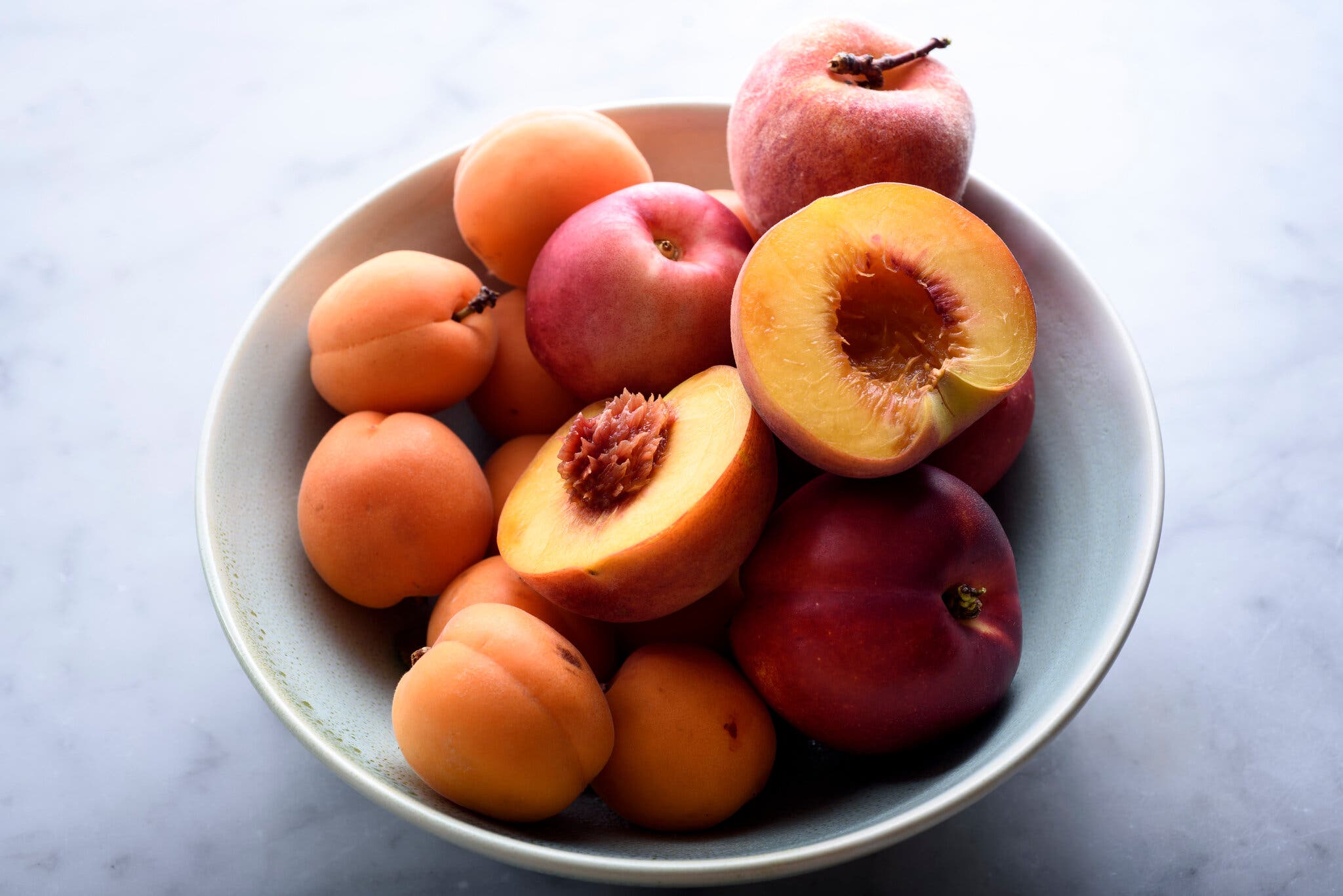 A bowl filled with fresh apricots, peaches and nectarines.